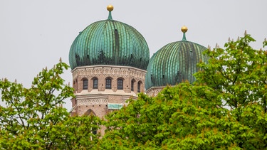 09.04.2024, Bayern, München: Die beiden Turmspitzen der Frauenkirche ragen über die Baumkronen am Viktualienmarkt. Foto: Peter Kneffel/dpa +++ dpa-Bildfunk +++ | Bild: dpa-Bildfunk/Peter Kneffel